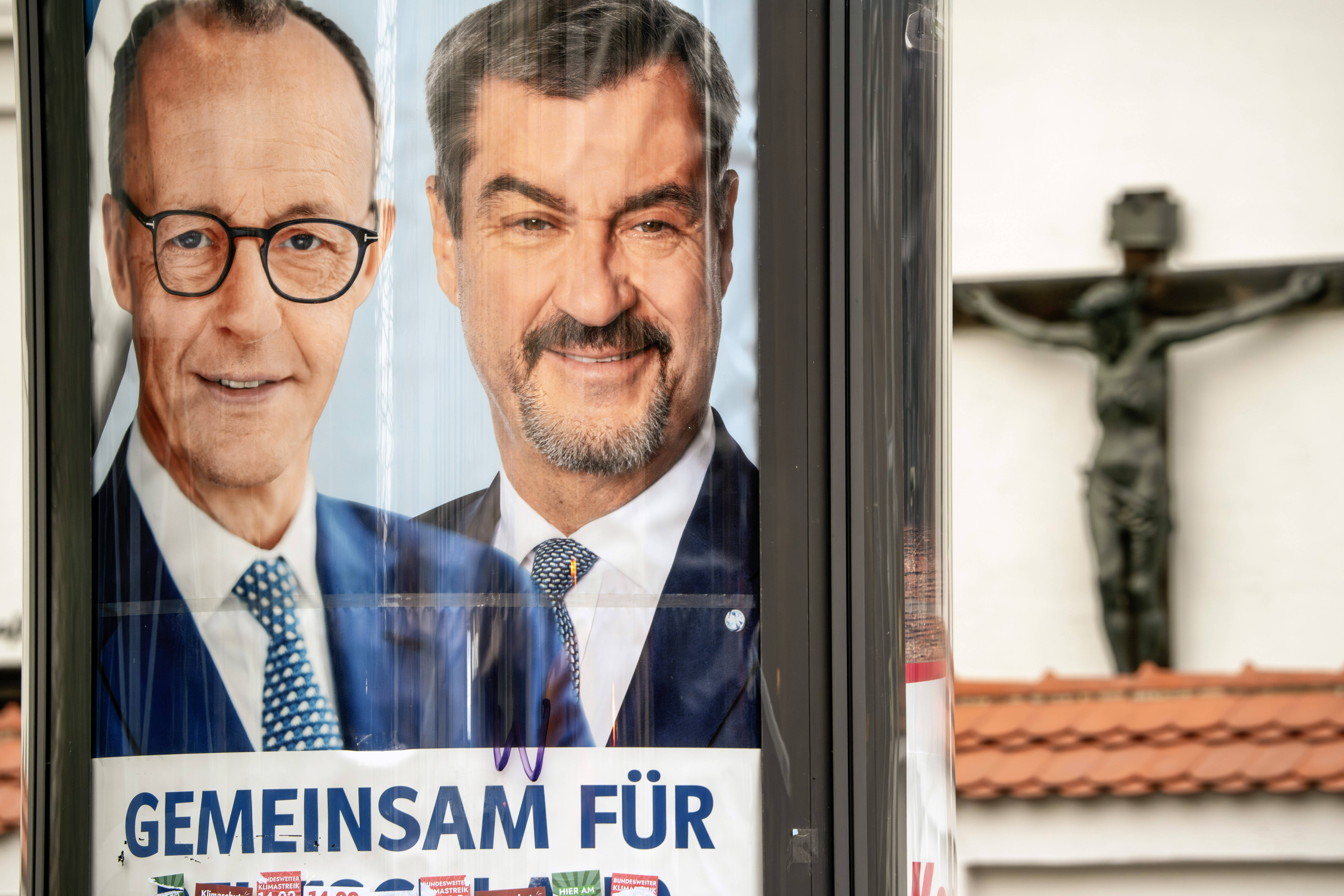 Die Spitzenkandidaten von CDU und CSU, Friedrich Merz und Markus Söder, auf einem Plakat zum Bundestagswahlkampf 2025 vor einem Kruzifix