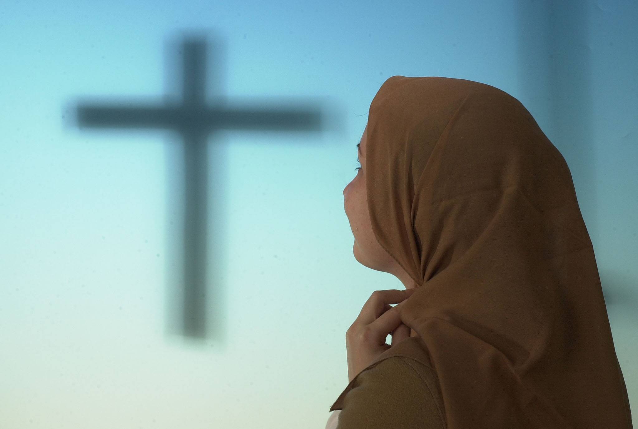 Moslemische Lehrerin mit Kopftuch, im Hintergrund das Kreuz Christi