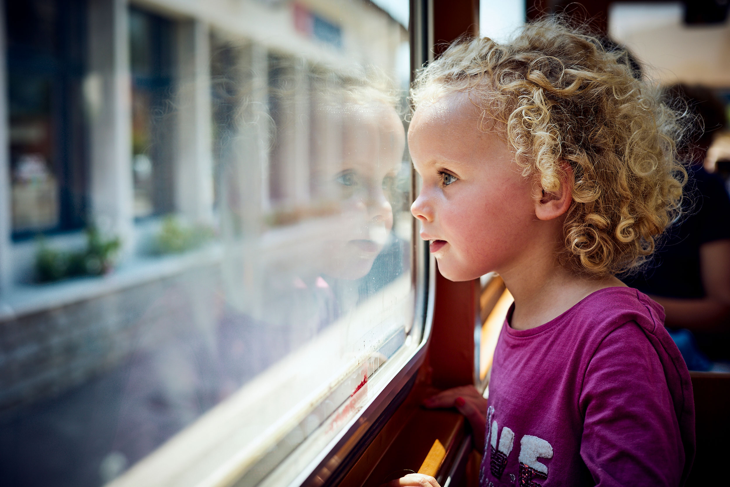 Töchterchen guckt aus dem Abteilfenster eines Zuges auf das Stationsgebäude, Sommer 2025