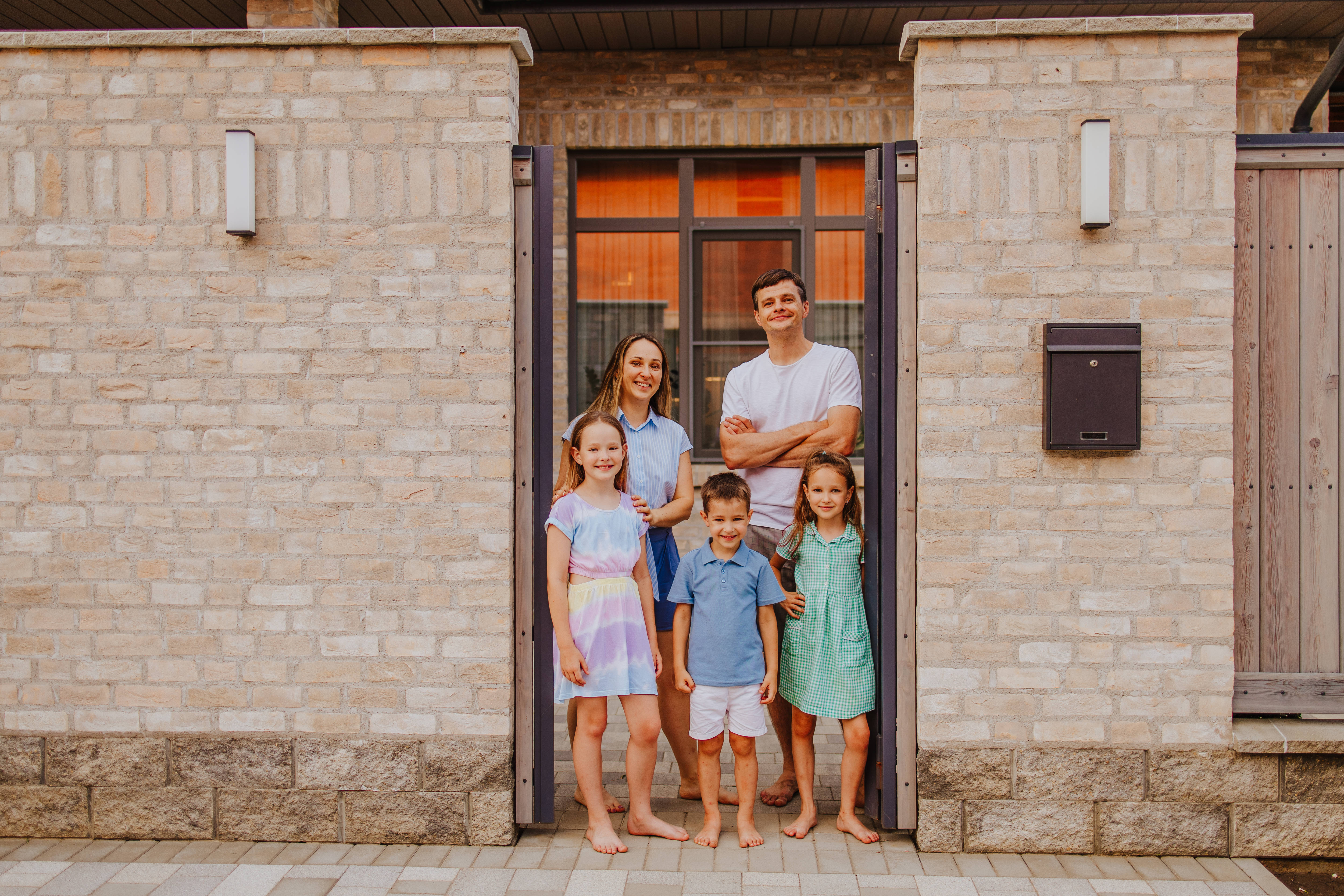 Eine fünfköpfige Familie steht barfuß in der hohen Umfriedung ihres Eigenheims, 2025