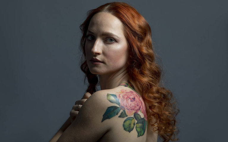 Junge, rothaarige Frau mit Blumen-Tattoo