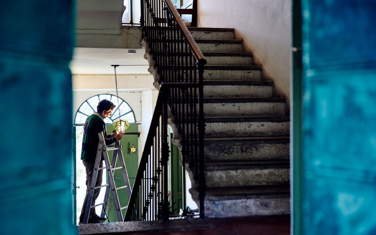 Oliver Stock beim Auswechseln der Glühbirne auf einer Leiter im Treppenhaus