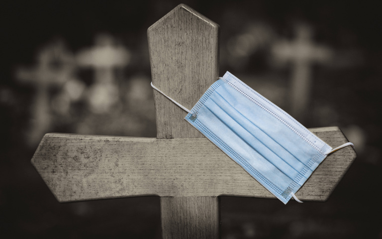 Eine Corona-Maske hängt an einem Grabkreuz