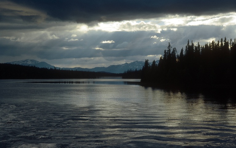 Sonnenstrahlen brechen durch schwarze Wolken über einem See bei Dikanäs in der historischen Provinz Lappland, Schweden