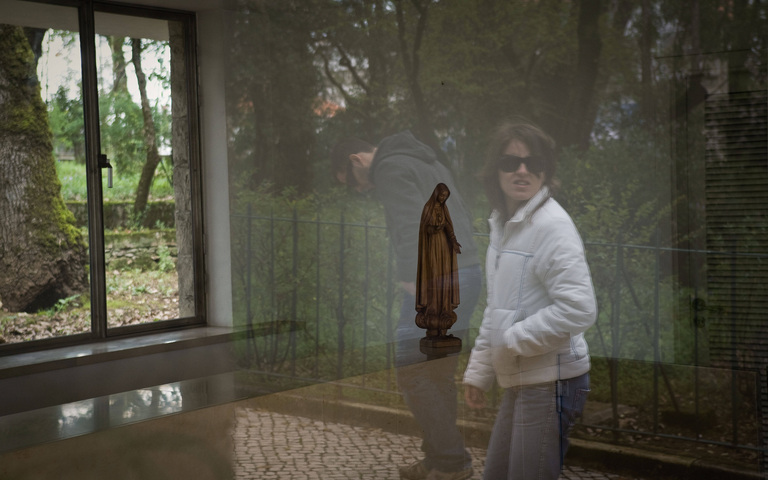 Pilger spiegeln sich in einer Scheibe, hinter der eine Marienstatue im Wallfahrtsort Fatima steht