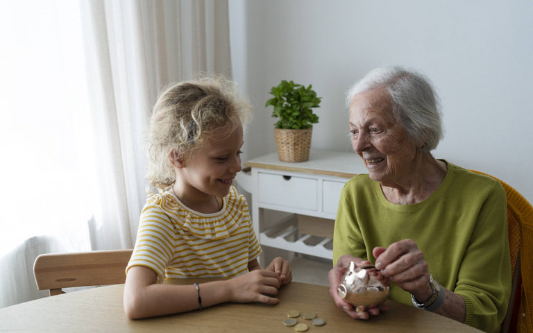 Großmutter und Enkelin werfen Geld in ein Sparschwein