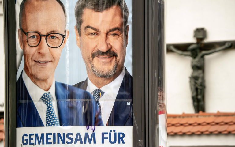 Die Spitzenkandidaten von CDU und CSU, Friedrich Merz und Markus Söder, auf einem Plakat zum Bundestagswahlkampf 2025 vor einem Kruzifix