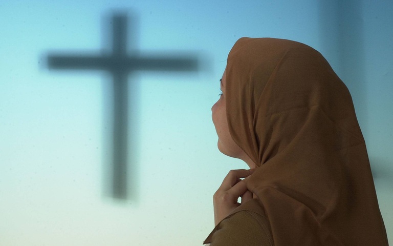 Moslemische Lehrerin mit Kopftuch, im Hintergrund das Kreuz Christi