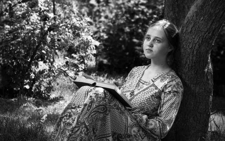 Junge Frau liest an einen Baum gelehnt im Wald ein Buch