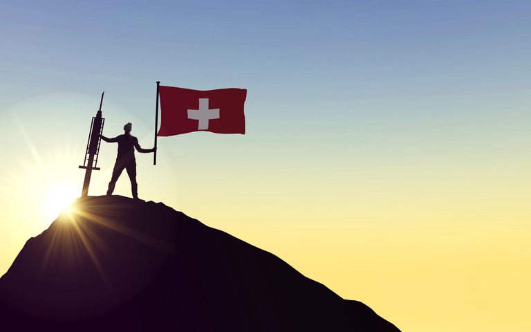 Mann mit Spritze und Schweizer Flagge auf Berggipfel